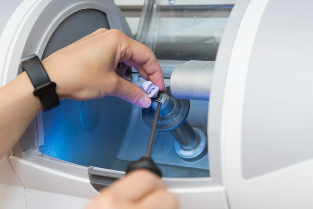 Hands taking a CEREC dental crown out of milling machine