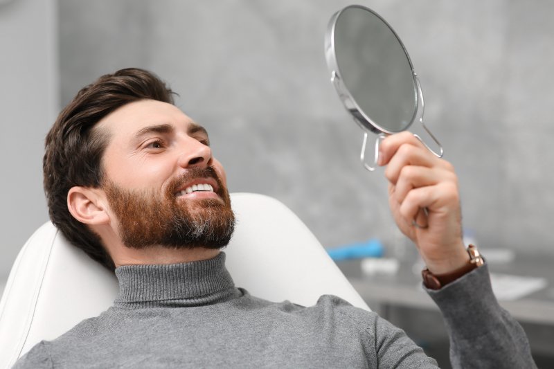 a man smiling in the mirror at new dental crown